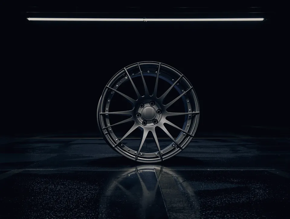 A forged multi-spoke wheel standing on a wet garage floor under a light bar